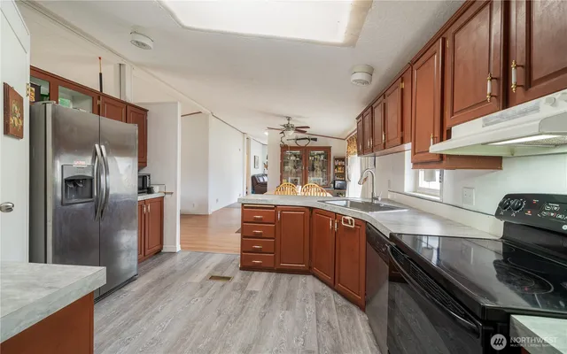 a kitchen with stainless steel appliances granite countertop a refrigerator a sink dishwasher a stove and white countertops with wooden floor