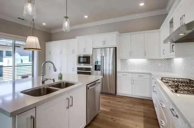 a kitchen with stainless steel appliances a sink dishwasher a refrigerator and a stove with wooden floors