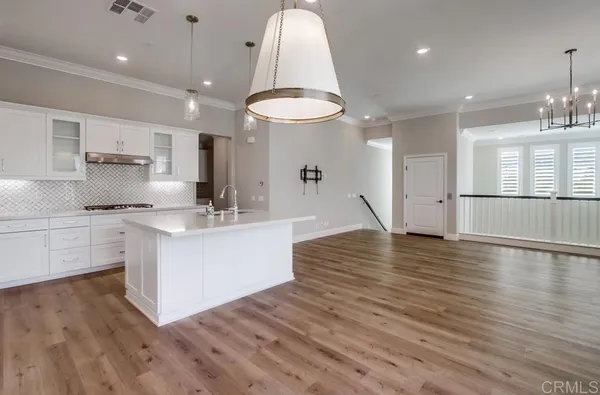 a large room with kitchen island a sink wooden floor white stainless steel appliances and cabinets