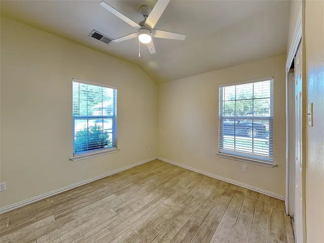 an empty room with wooden floor fan and windows