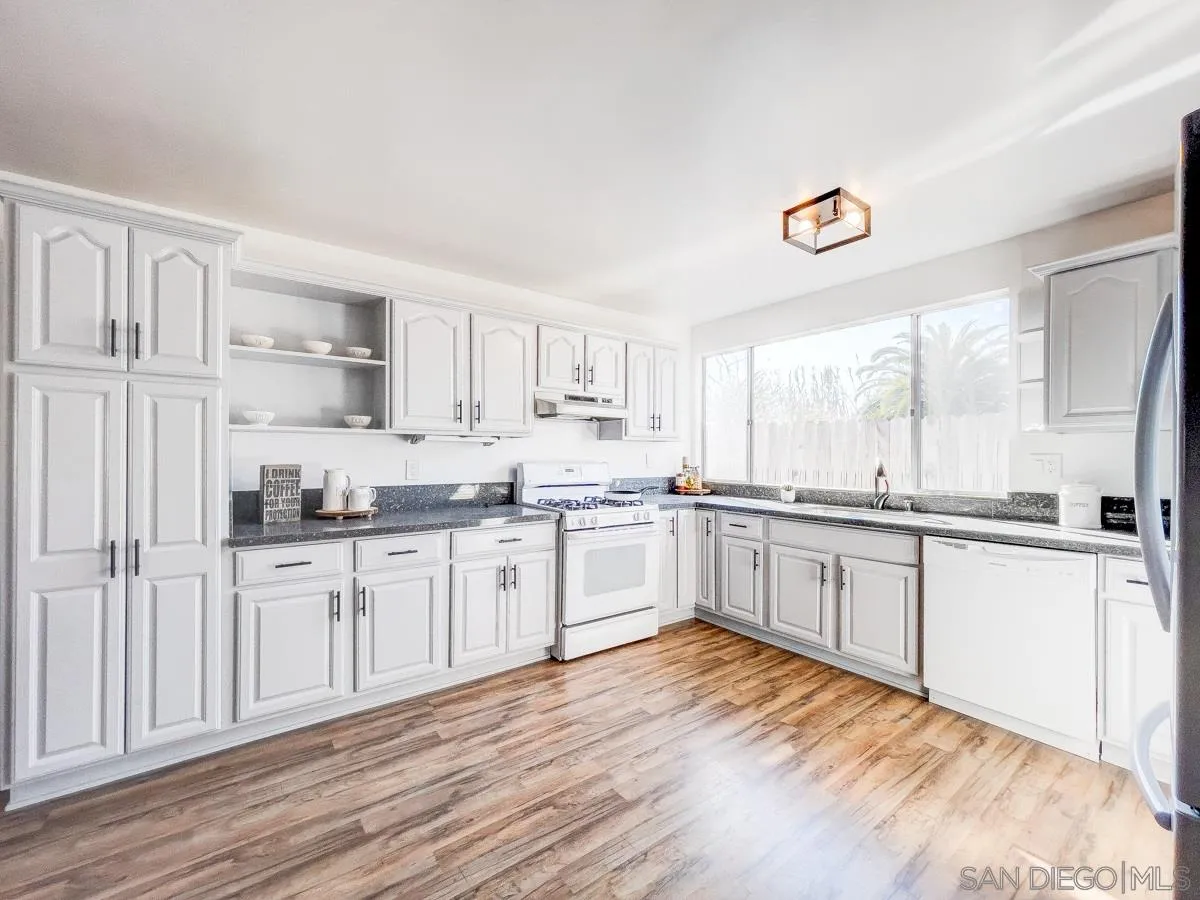 2922 Luana Drive Oceanside, CA 92056 - Photo 8 of 28 a large white kitchen with granite countertop a stove a sink and dishwasher with wooden floor
