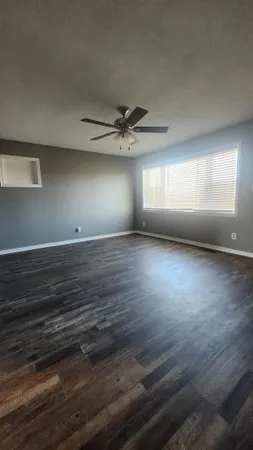 an empty room with wooden floor and windows with curtains