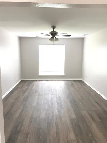 an empty room with wooden floor ceiling fan and windows