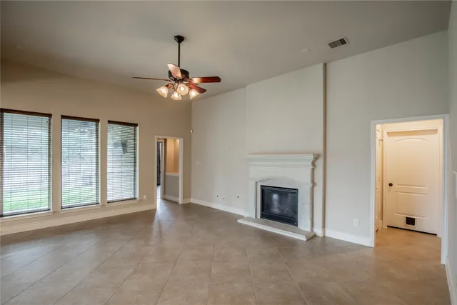 a view of an empty room with chandelier fan and fire place