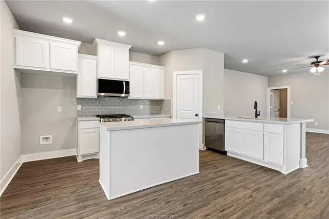 a kitchen with kitchen island microwave stove refrigerator and white cabinets with wooden floor