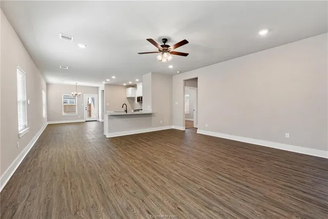 a view of an empty room and kitchen with wooden floor and a ceiling fan