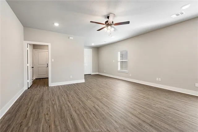 a view of an empty room with wooden floor and a ceiling fan