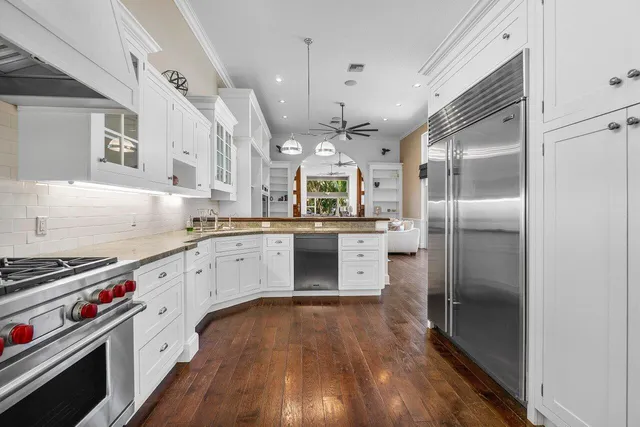 a kitchen with stainless steel appliances a refrigerator a sink dishwasher a stove and white cabinets with wooden floor