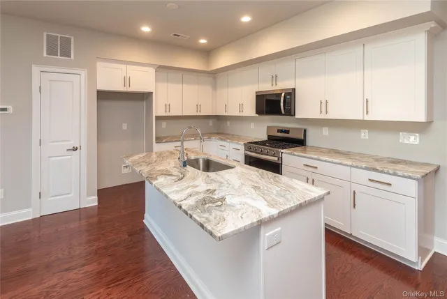 a kitchen with stainless steel appliances granite countertop a stove top oven a refrigerator a sink and white cabinets with wooden floor