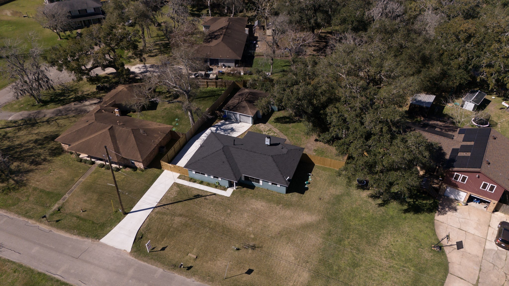 407 Tamarind Street Lake Jackson, TX 77566 - Photo 3 of 36 The property features a large driveway and a fenced backyard, surrounded by mature trees. It's situated in a quiet suburban neighborhood with nearby houses and greenery.