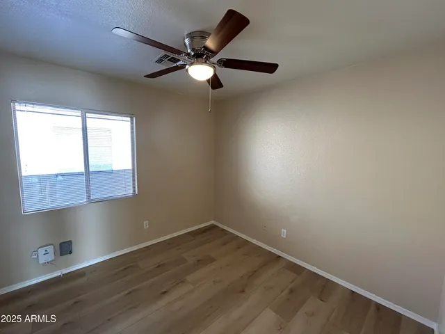 an empty room with wooden floor fan and windows