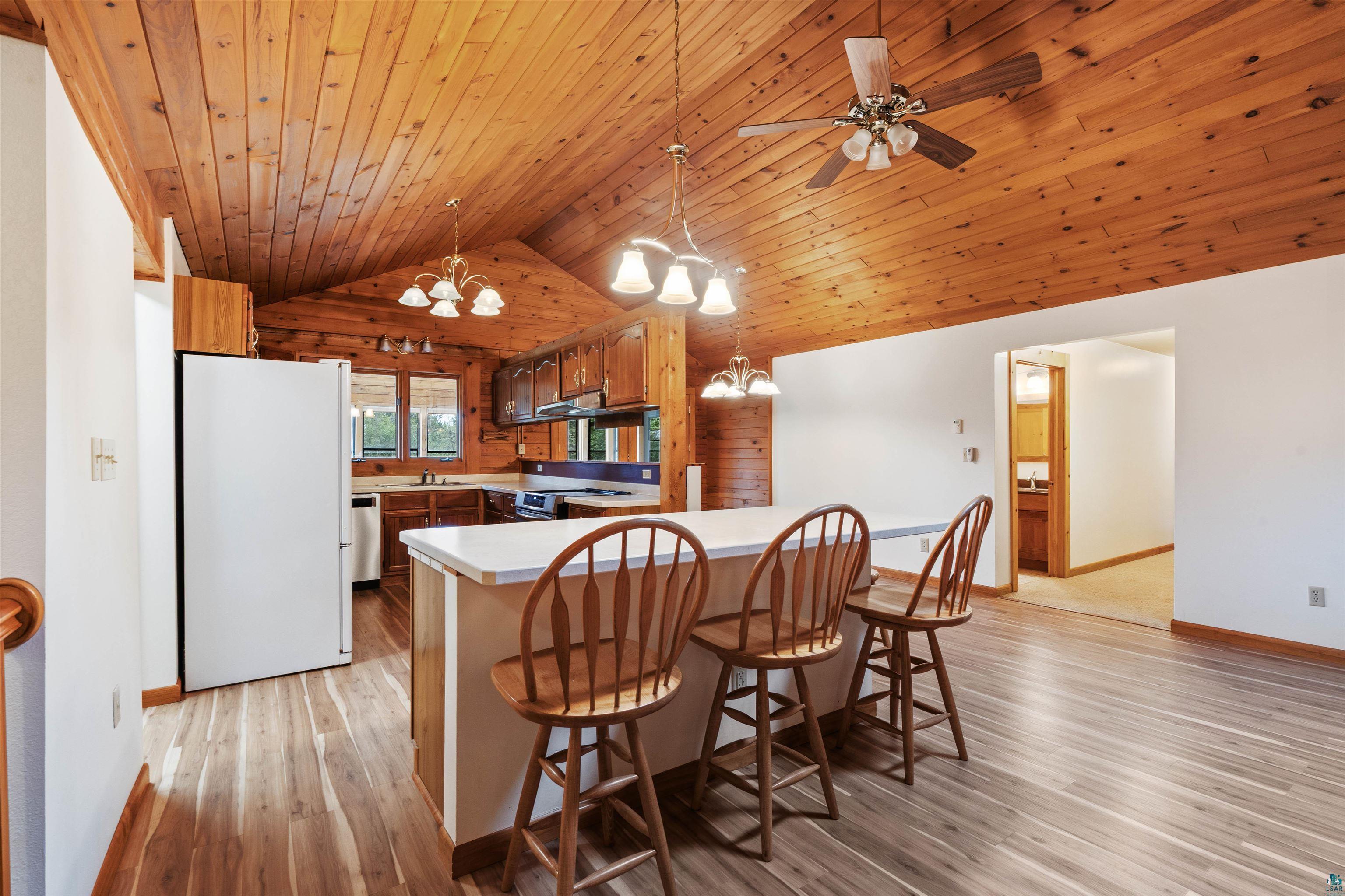 5373 Lester River Road Duluth, MN 55804 - Photo 11 of 39 Vaulted wood-paneled ceiling, wood-finish flooring, white countertops, built-in kitchen cabinetry, and ceiling fan with integrated lighting