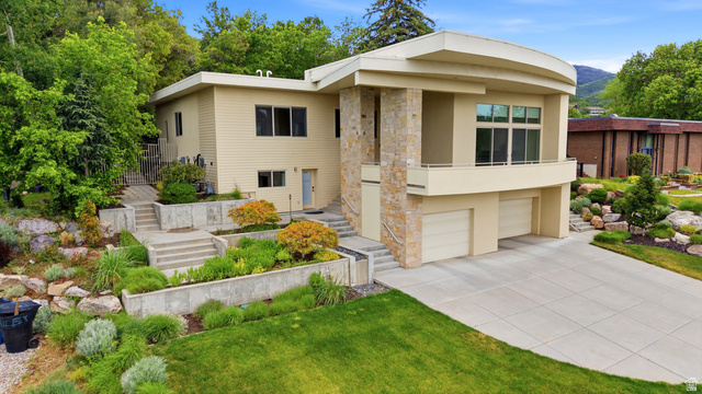 Contemporary architectural exterior featuring stone veneer accents, an integrated two-car garage, multiple windows, and a curved balcony