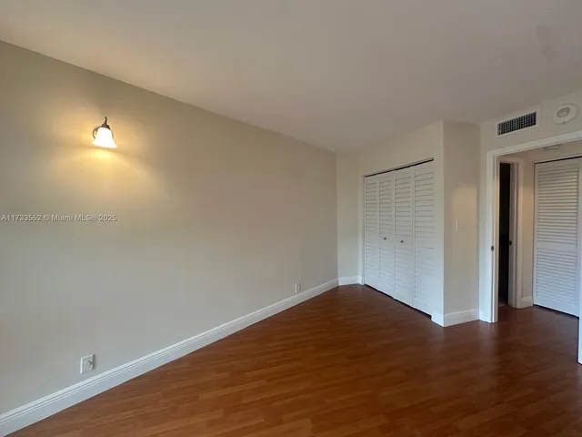 a view of an empty room with wooden floor and closet