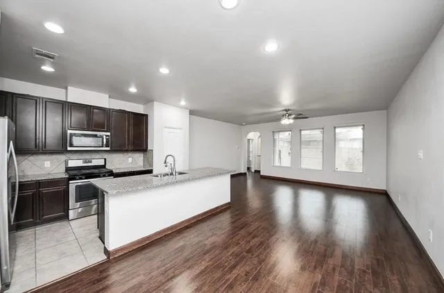 a large kitchen with stainless steel appliances a large counter top a stove a sink dishwasher and a refrigerator with wooden floor