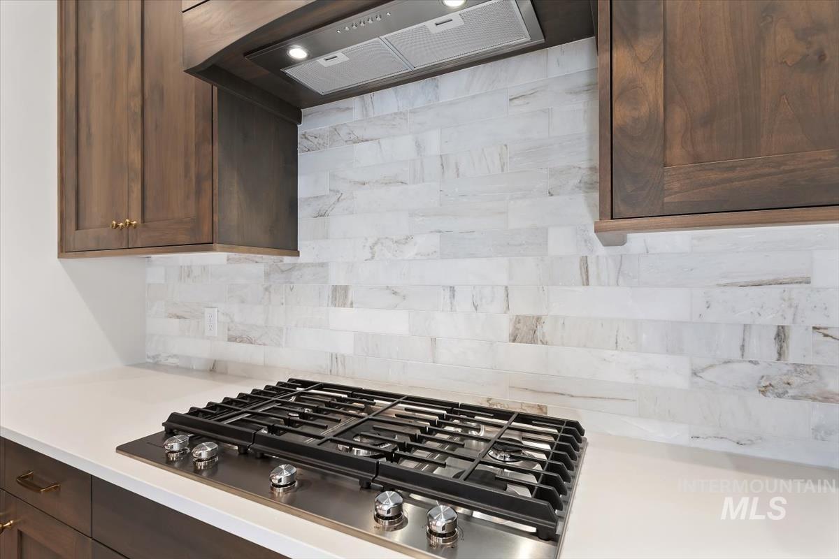 2147 East Blakehurst Avenue Kuna, ID 83634 - Photo 13 of 43 Kitchen with premium range hood, stainless steel gas stovetop, dark brown cabinets, backsplash, and light stone countertops