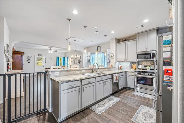 a kitchen with stainless steel appliances granite countertop a stove top oven a sink dishwasher and a refrigerator with wooden floor