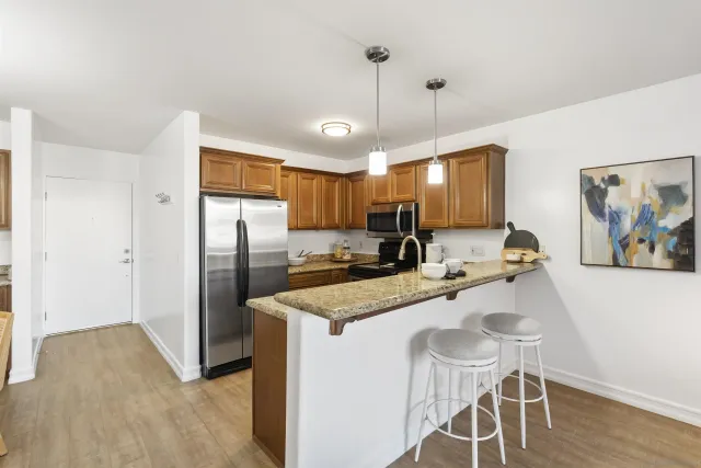 a kitchen with stainless steel appliances granite countertop a stove a refrigerator a sink a dining table and chairs with wooden floor