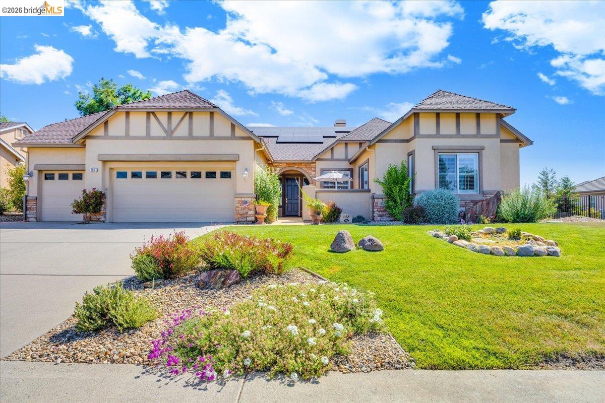 Stucco exterior with decorative exposed rafters and stone accents, featuring a multi-car garage, paved driveway, and established landscaping