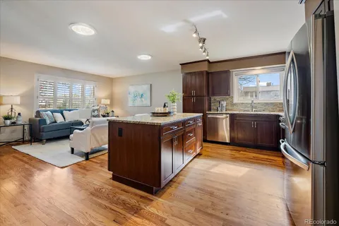 a kitchen with stainless steel appliances granite countertop a stove a sink dishwasher a refrigerator and a dining table with wooden floor