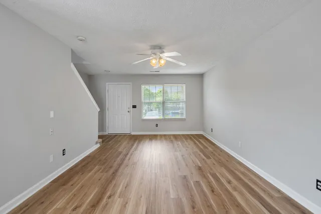 an empty room with wooden floor chandelier fan and windows