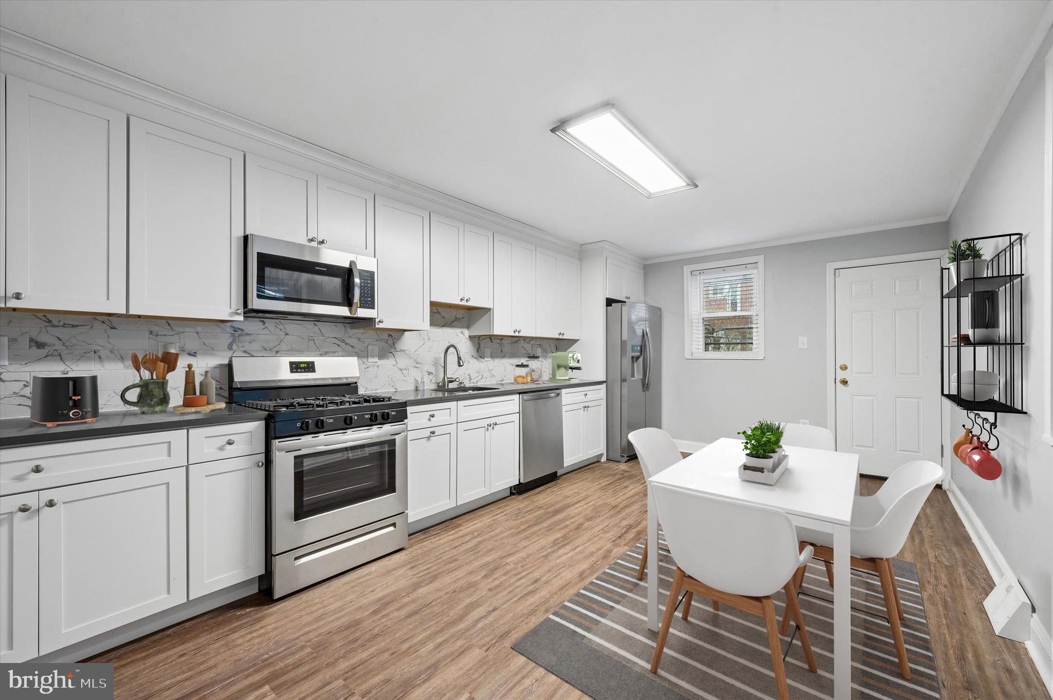 6129 Spruce Street Philadelphia, PA 19139 - Photo 6 of 18 a kitchen with stainless steel appliances a stove a sink dishwasher a microwave oven a dining table and chairs with wooden floor