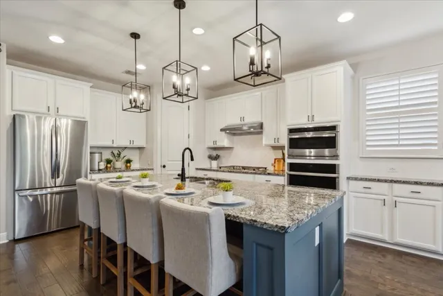 a kitchen with stainless steel appliances granite countertop a sink a stove a refrigerator cabinets and chairs