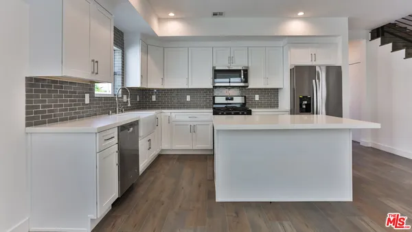 a kitchen with stainless steel appliances a sink stove refrigerator and white cabinets with wooden floor