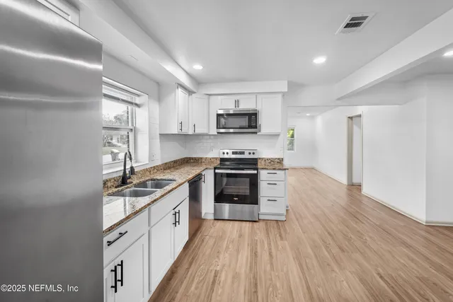 a kitchen with stainless steel appliances a stove top oven a sink a refrigerator white cabinets and wooden floor