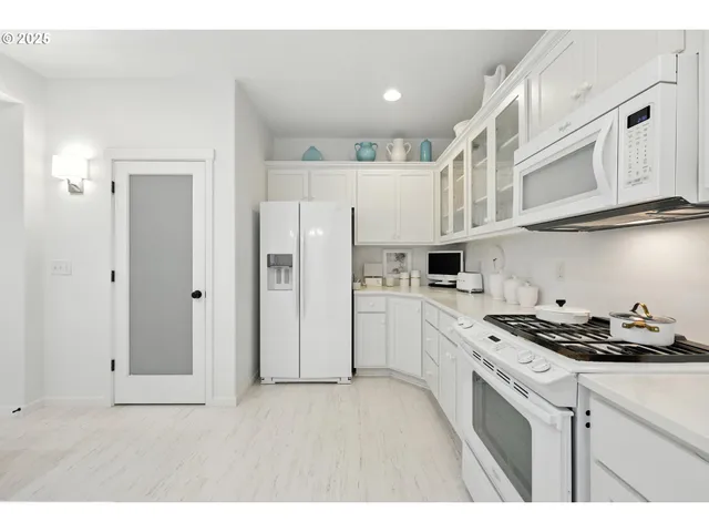 a kitchen with stainless steel appliances granite countertop a refrigerator a stove a sink and white cabinets with wooden floor