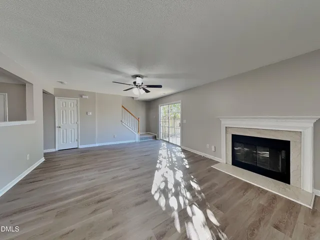 a view of an empty room with wooden floor fireplace and a window