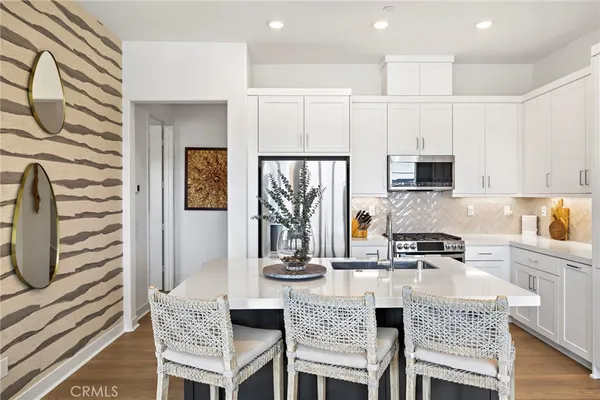 a kitchen with stainless steel appliances granite countertop a stove a sink a microwave a refrigerator white cabinets and couches with wooden floor