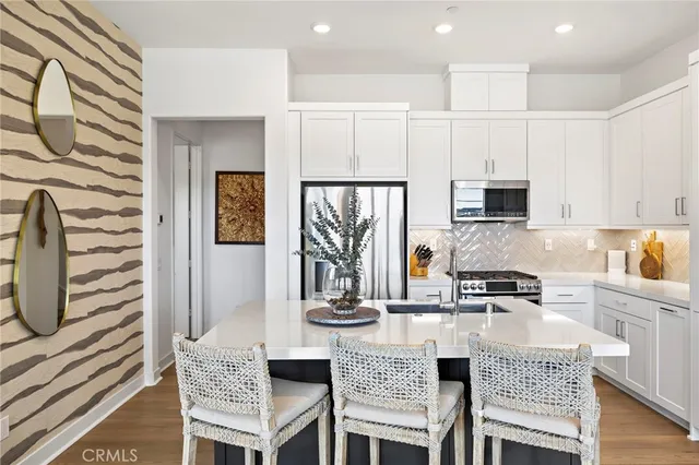 a kitchen with stainless steel appliances granite countertop a stove a sink a microwave a refrigerator white cabinets and couches with wooden floor