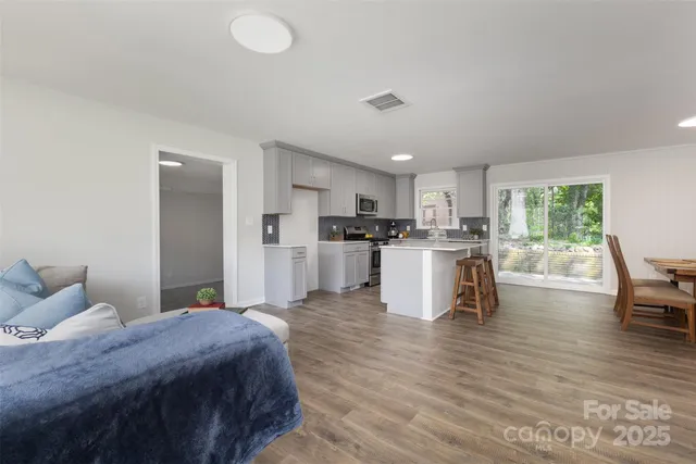 a kitchen with stainless steel appliances granite countertop a stove top oven a sink dishwasher a dining table and chairs with wooden floor