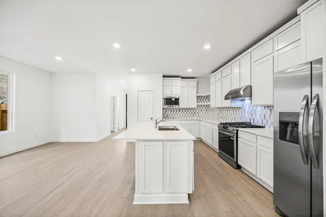 a kitchen with stainless steel appliances granite countertop a stove top oven a refrigerator a sink and dishwasher with wooden floor