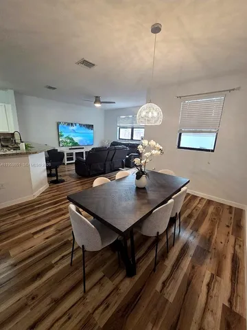 a view of a dining room and livingroom with furniture wooden floor a rug a painting and a chandelier