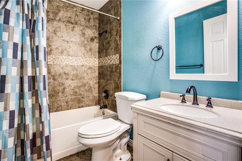 6817 Haltom Road Fort Worth, TX 76137 - Photo 6 of 25 Bathroom featuring a white vanity with an undermount sink and a light-toned countertop, dark-finished hardware, a framed mirror, and a shower/tub combination with tiled surround and decorative accent band