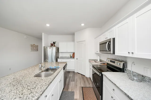 a kitchen with stainless steel appliances granite countertop a stove top oven a sink a refrigerator and white cabinets with wooden floor