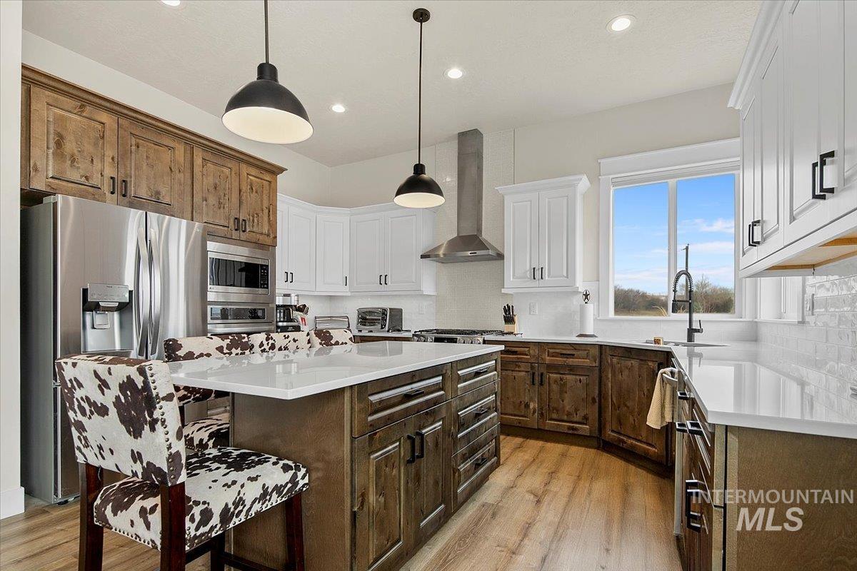 6721 El Paso Road Caldwell, ID 83607 - Photo 17 of 50 Kitchen with dark brown cabinets, a kitchen island, hanging light fixtures, appliances with stainless steel finishes, and light wood finished floors