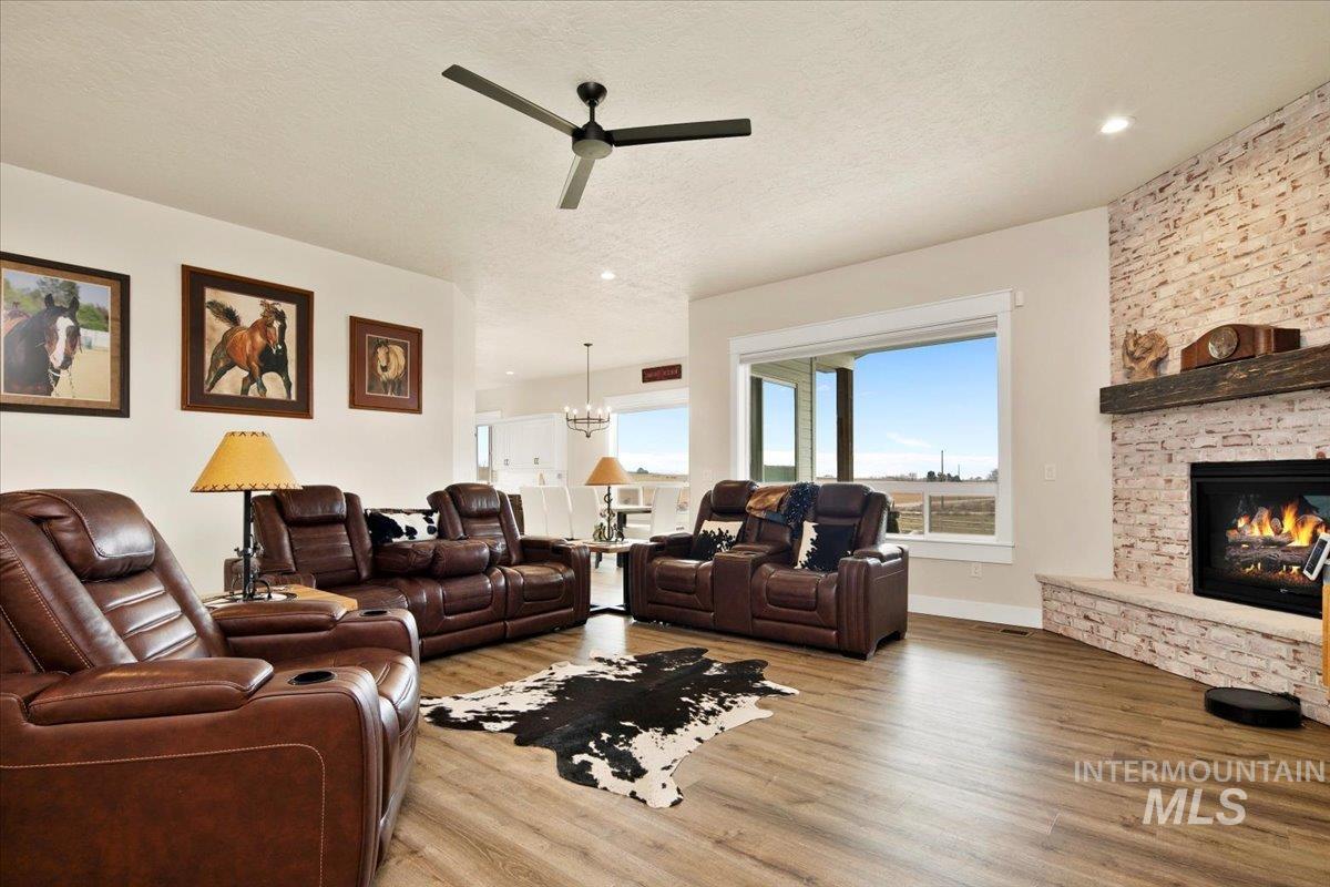 6721 El Paso Road Caldwell, ID 83607 - Photo 9 of 50 Living room featuring light wood finished floors, a stone fireplace, a chandelier, a textured ceiling, and a ceiling fan