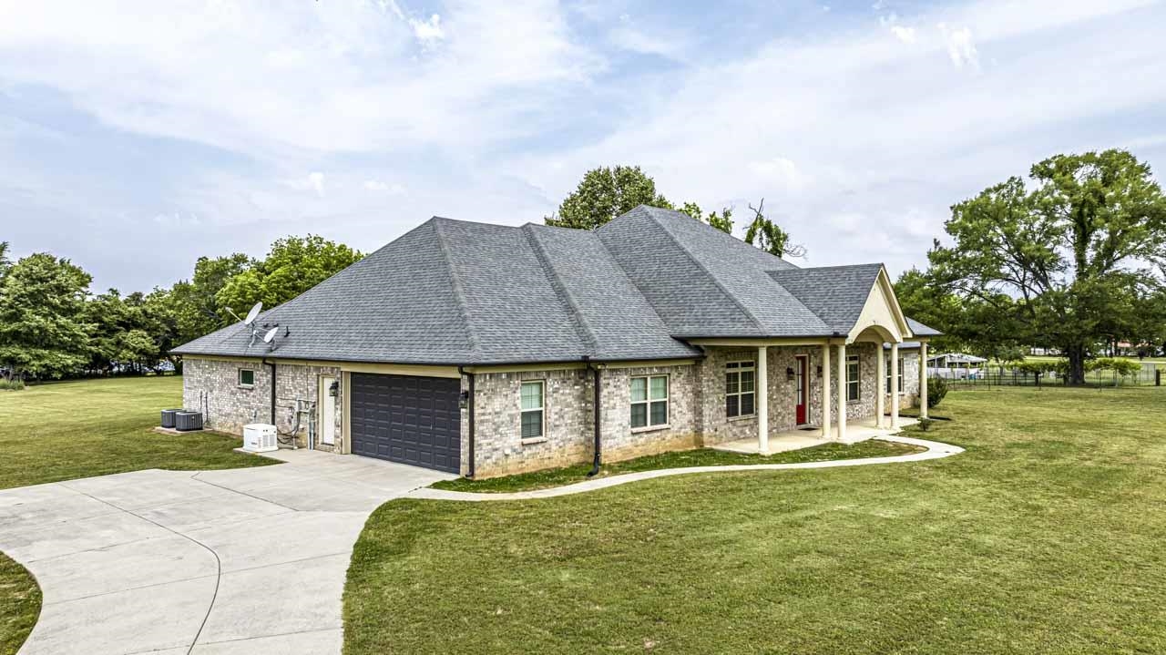 185 Belmont Road Mason, TN 38049 - Photo 32 of 38 Brick exterior with a gray shingle roof, featuring an attached garage with a dark panel door, a concrete driveway, and a covered front porch with white columns