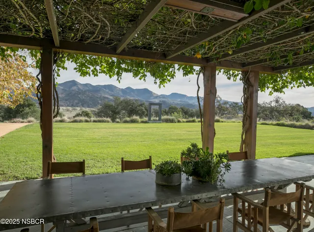 a view of a patio with lawn chairs under an umbrella next to a yard