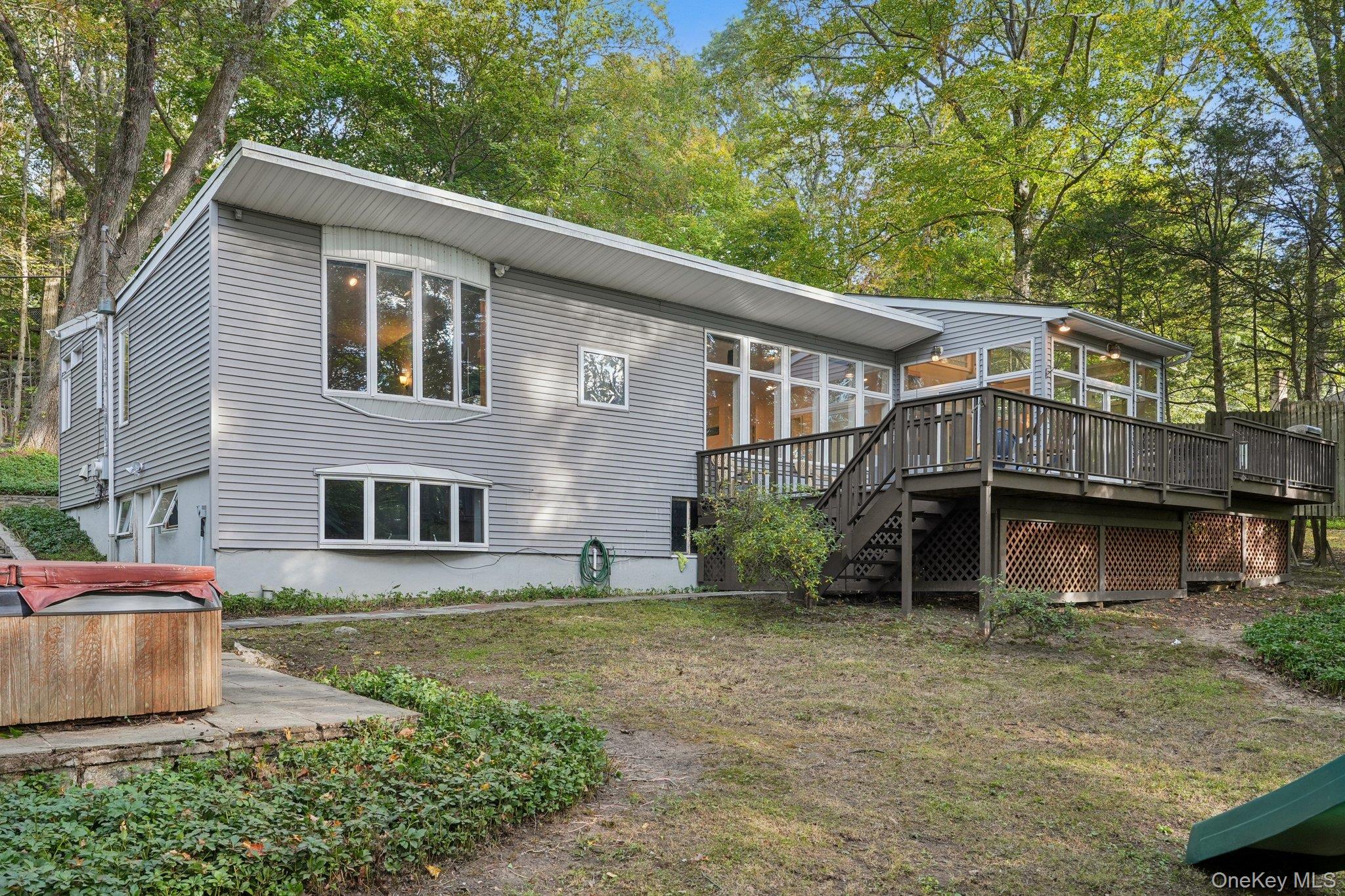 Back of house featuring stairway, view of scattered trees, a hot tub, a wooden deck, and a sunroom