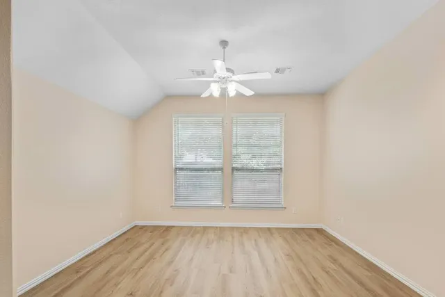 an empty room with wooden floor chandelier fan and windows