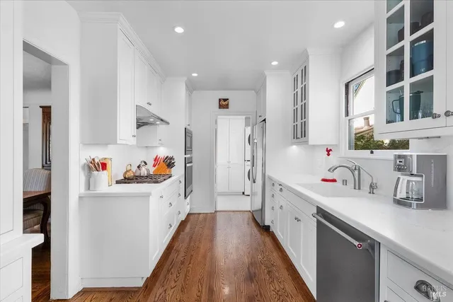 a kitchen with stainless steel appliances a sink a stove a refrigerator cabinets and a dining table