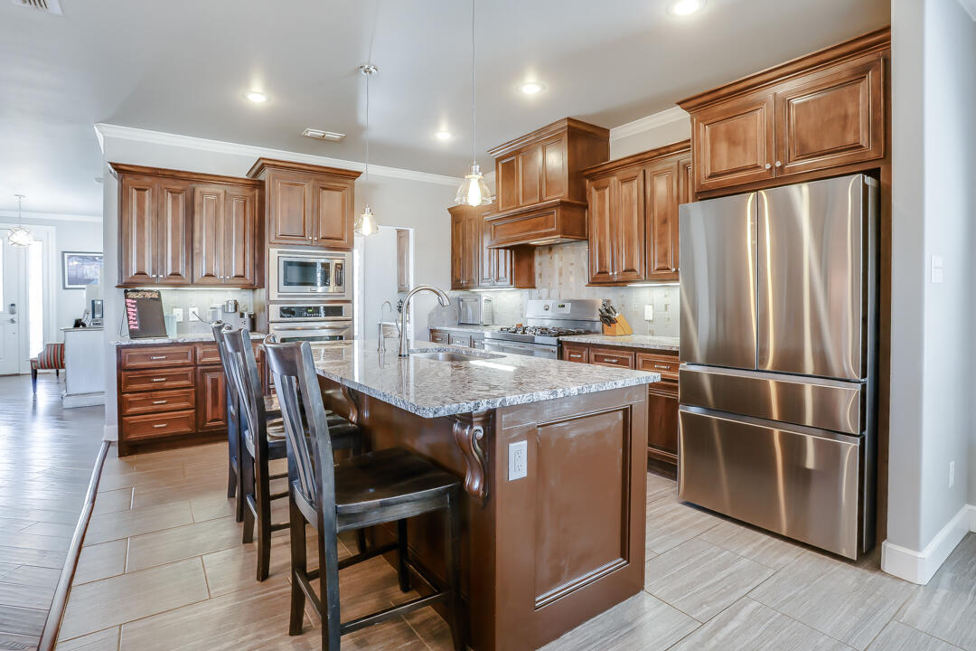 4712 121st Street Lubbock, TX 79424 - Photo 8 of 46 a kitchen with stainless steel appliances granite countertop a stove a refrigerator a kitchen island and chairs with wooden floor
