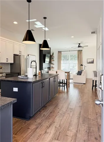 a open kitchen with stainless steel appliances granite countertop a stove a sink dishwasher a refrigerator and a dining table with wooden floor