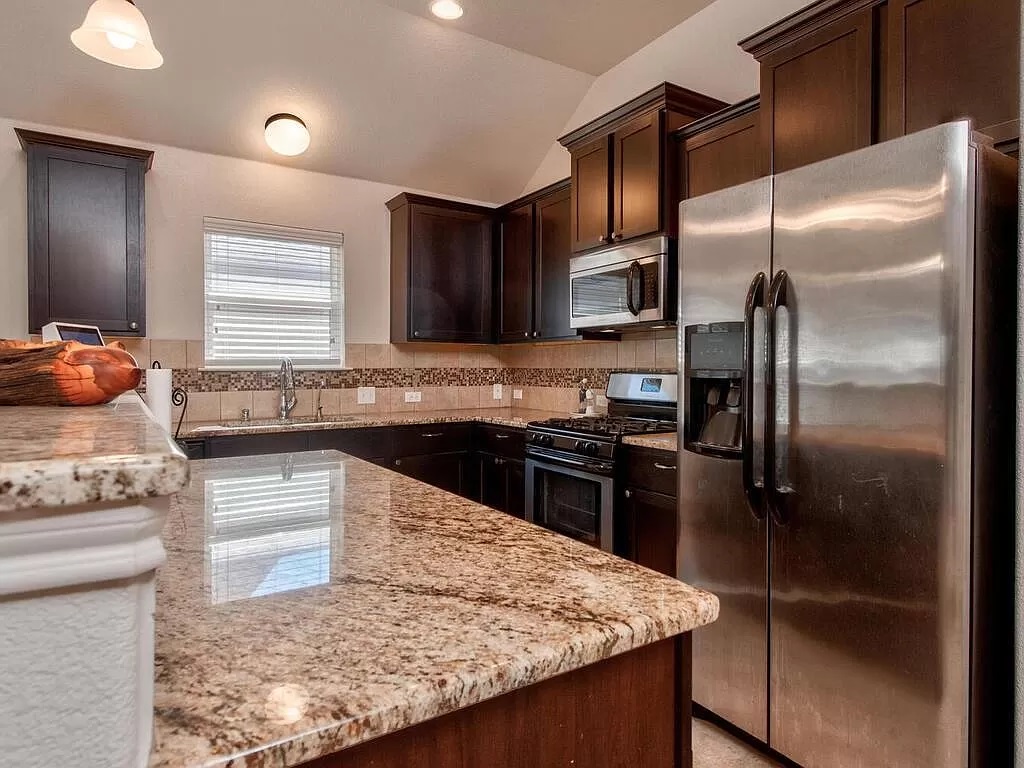 8217 Reggio Street Round Rock, TX 78665 - Photo 11 of 27 Kitchen with stainless steel appliances, light stone countertops, dark brown cabinetry, backsplash, and lofted ceiling
