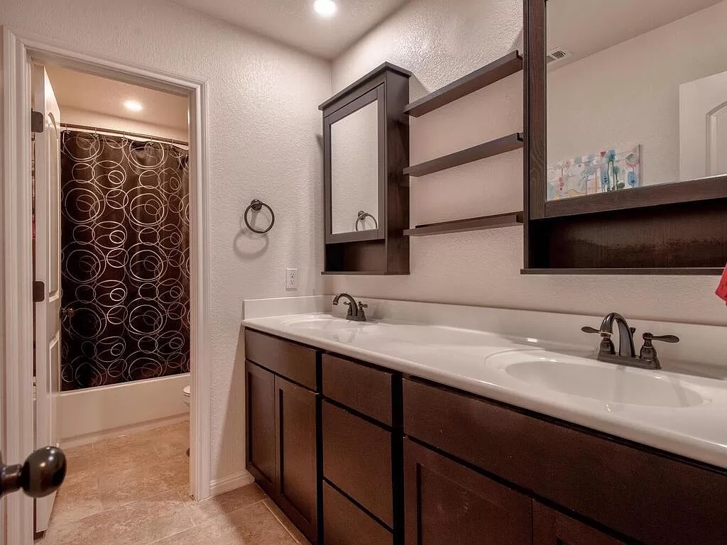 8217 Reggio Street Round Rock, TX 78665 - Photo 18 of 27 Full bath with a textured wall, double vanity, shower / bath combo with shower curtain, and light tile patterned flooring