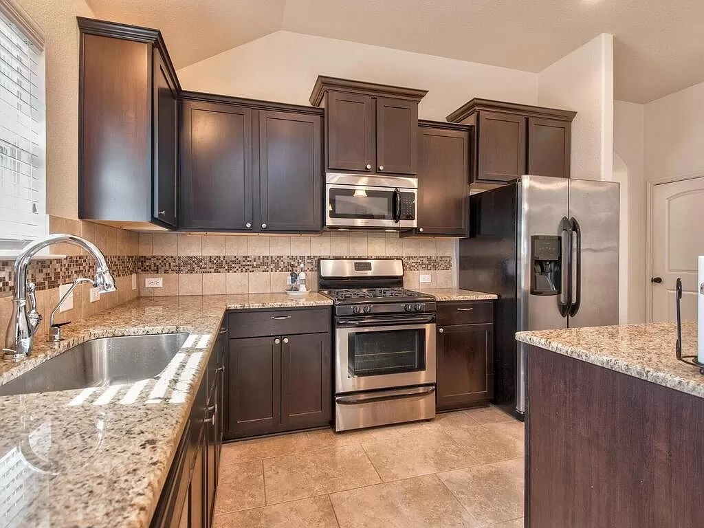 8217 Reggio Street Round Rock, TX 78665 - Photo 10 of 27 Kitchen featuring appliances with stainless steel finishes, tasteful backsplash, light stone countertops, dark brown cabinets, and light tile patterned flooring